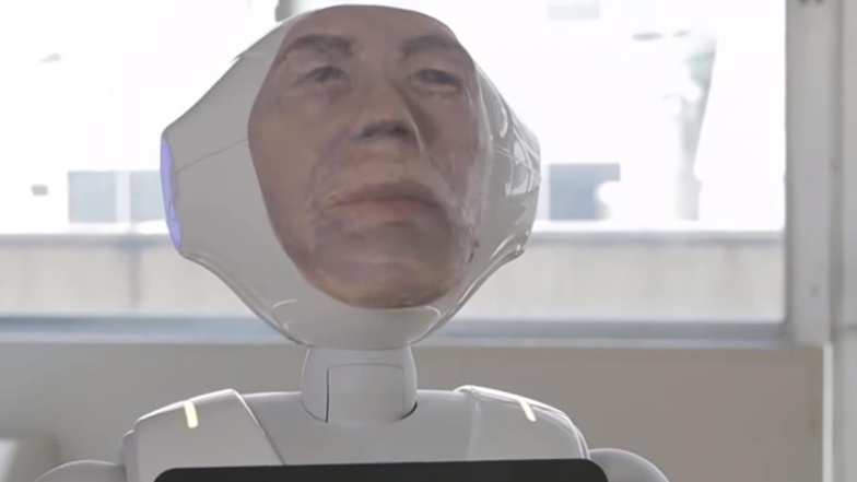 Le robot japonais Digital Shaman, avec le visage du défunt imprimé en 3D, permettrait d’aider à faire son travail de deuil (capture d’écran). Le robot japonais Digital Shaman, avec le visage du défunt imprimé en 3D, permettrait d’aider à faire son travail de deuil (capture d’écran).
