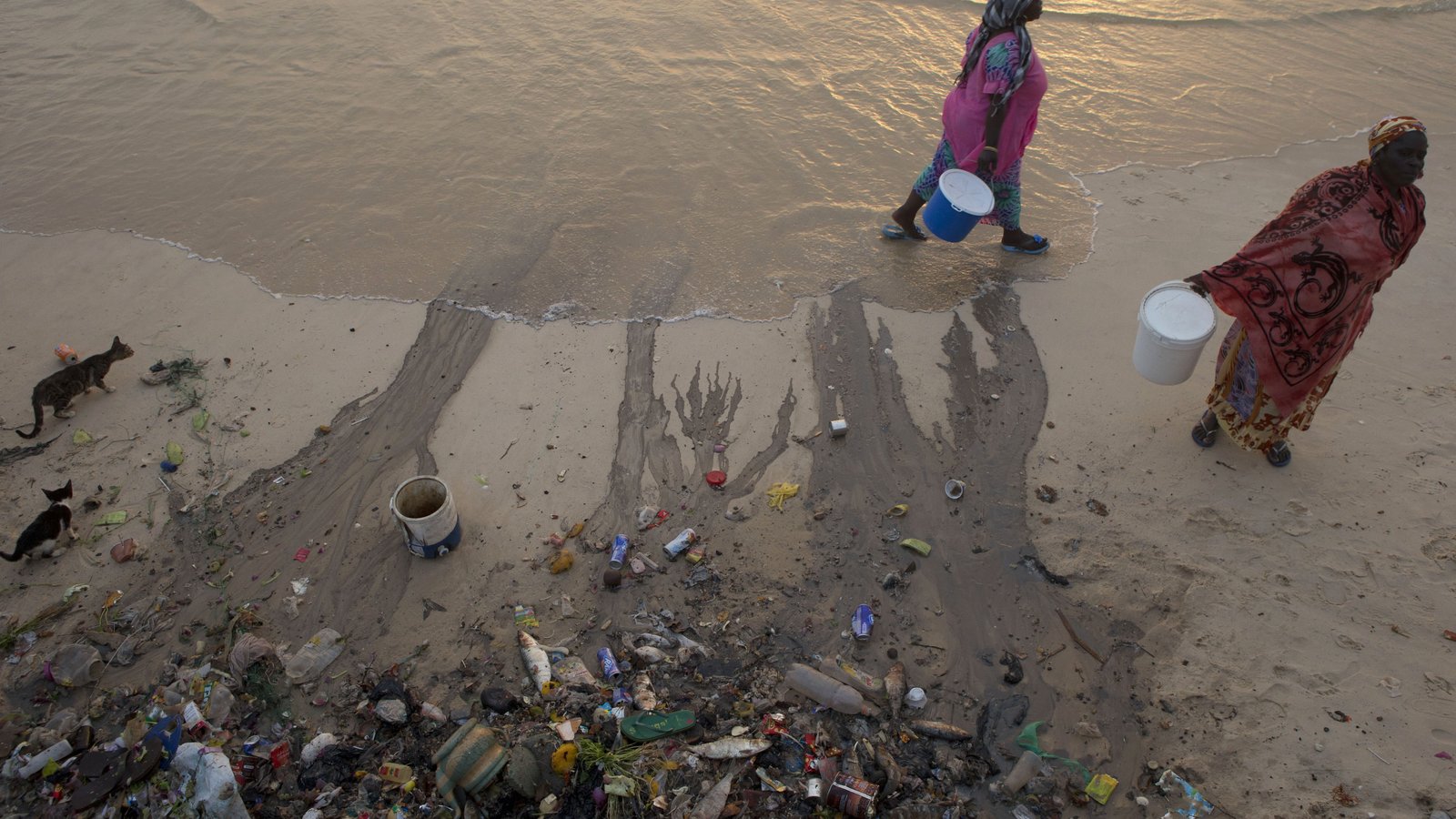 Woman walk past an area where local residents dump their household trash to be carried out by the tide, along the Atlantic Ocean in Saint-Louis, Senegal, Sunday, May 19, 2013. | AP Photo/Rebecca Blackwell